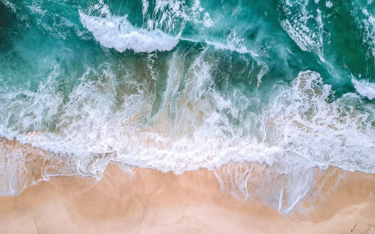 Olas rompiendo en una playa de arena, vistas desde el aire
