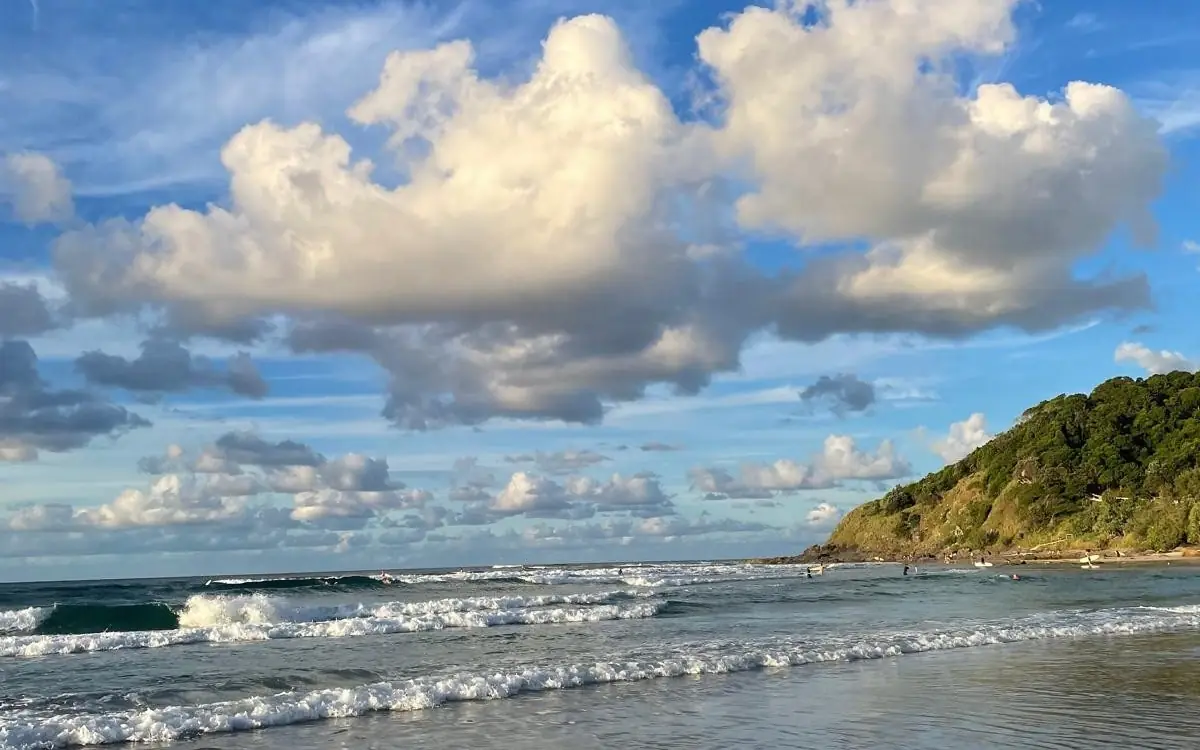 Playa con olas y grandes nubes blancas junto a un cabo verde