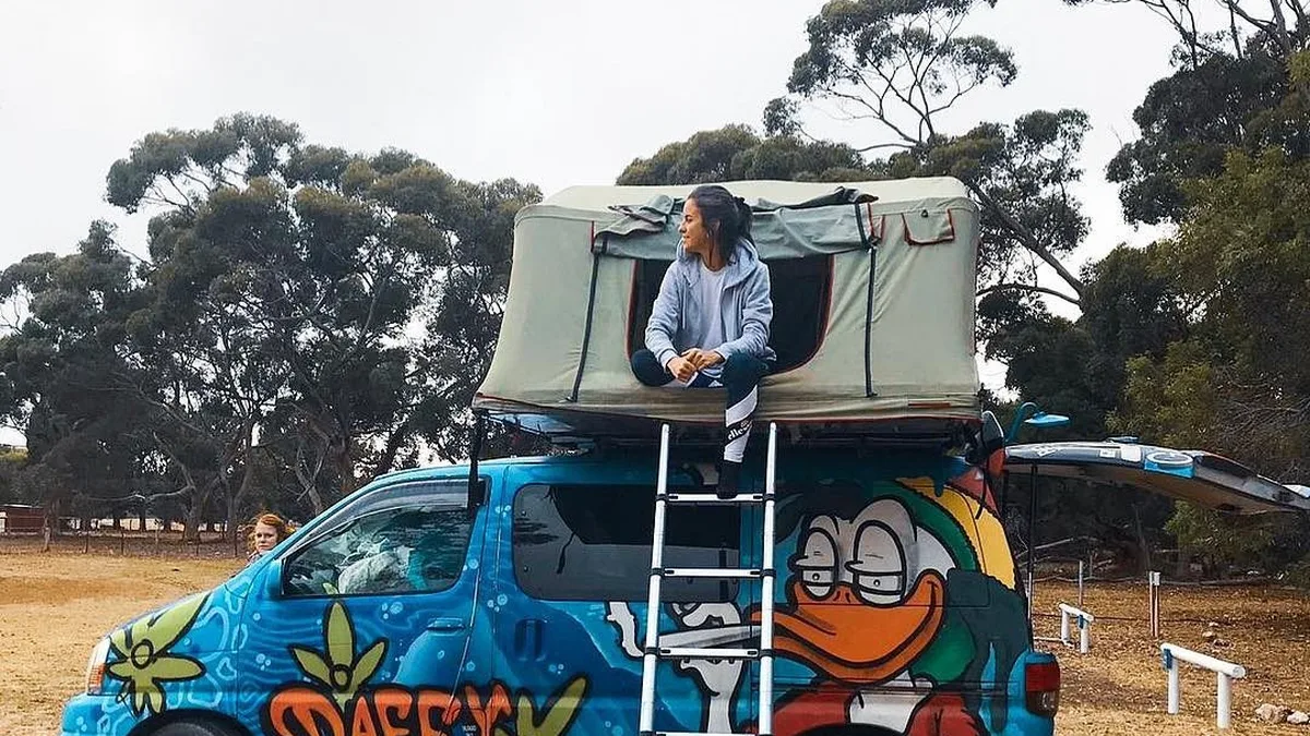 Estudiante sentada en la tienda de campaña del techo de una furgoneta de colores en Australia