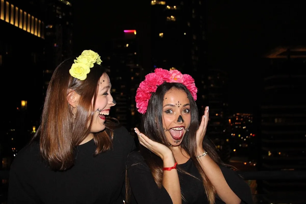 Dos estudiantes de Salta maquilladas de catrina con coronas de flores, de noche en la ciudad