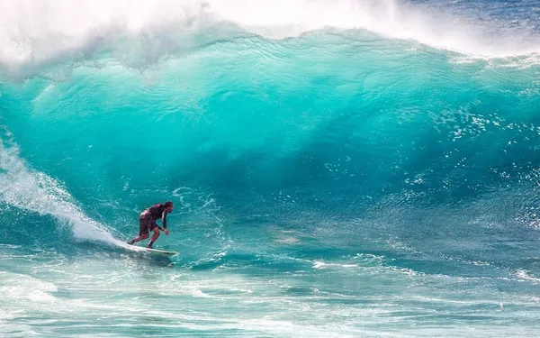 Surfista en una ola enorme de agua turquesa
