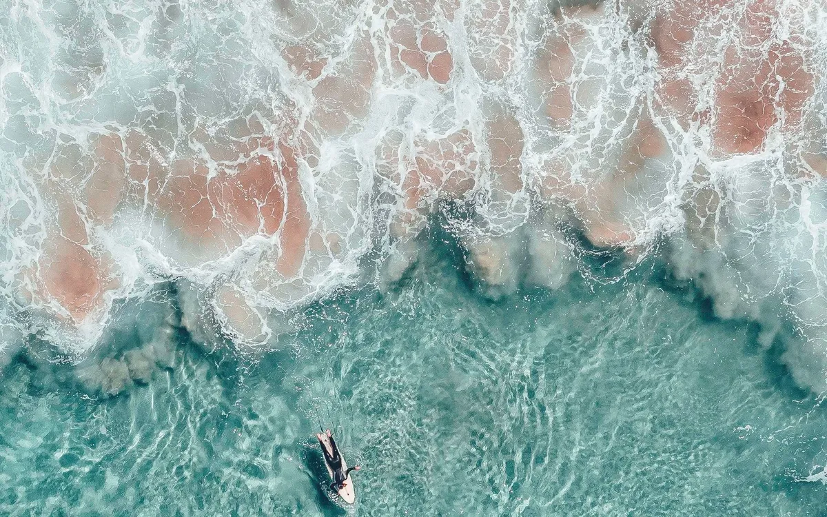 Surfistas en el agua turquesa de una playa australiana, vistos desde el aire