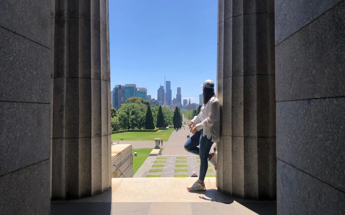 Estudiante entre las columnas del Shrine of Remembrance, con el centro de Melbourne al fondo