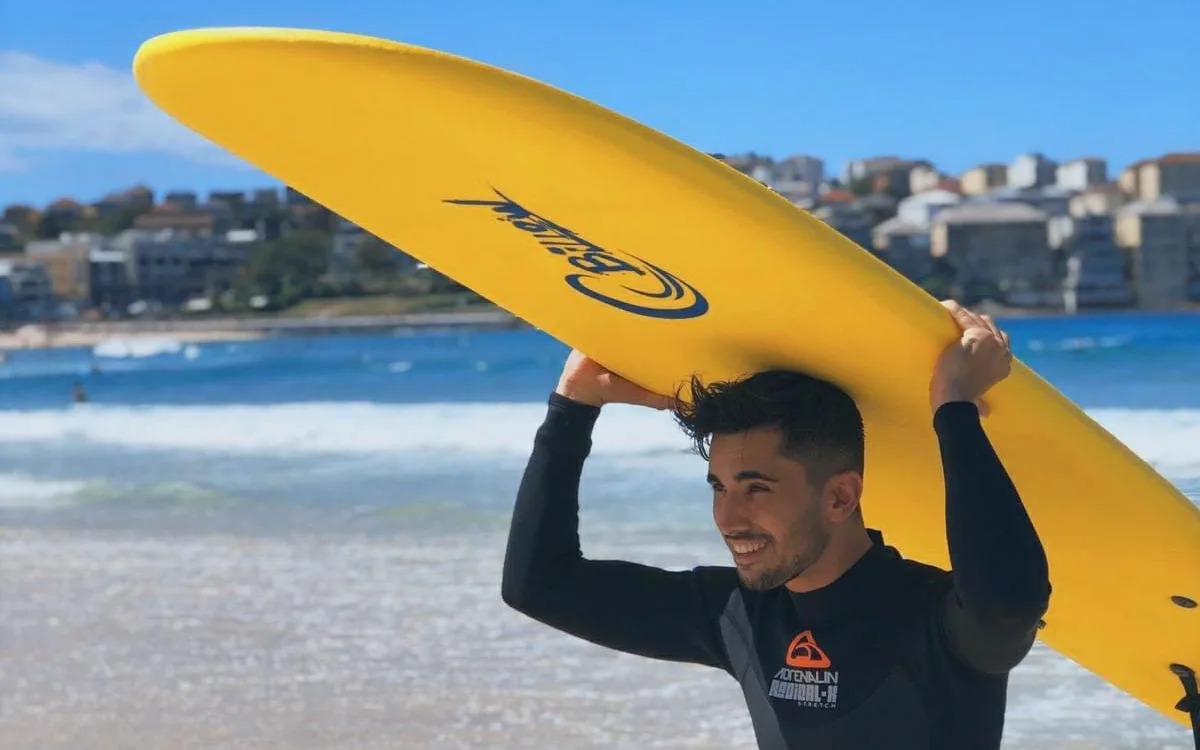 Estudiante con una tabla de surf amarilla sobre la cabeza en la playa de Bondi, en Sydney
