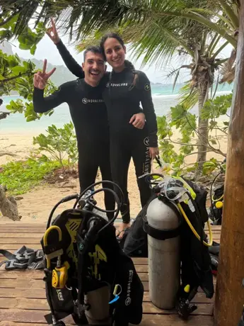 Pareja con trajes de buceo junto a sus equipos, bajo las palmeras