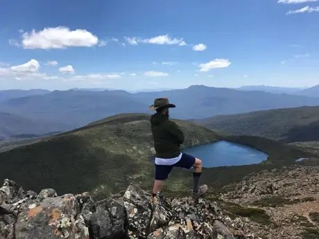 Estudiante en lo alto de un mirador de montaña, con un lago al fondo