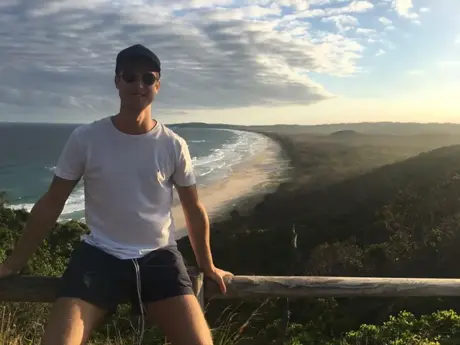 Estudiante sentado en la barandilla de un mirador sobre la costa