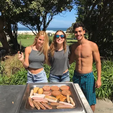 Tres amigos junto a una barbacoa en un parque, con el mar al fondo
