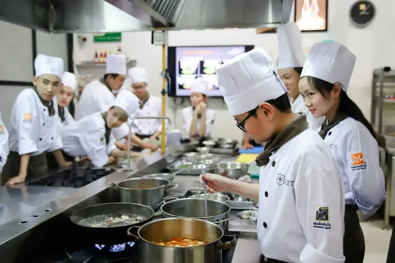 Estudiantes de cocina con gorro de chef en una cocina profesional