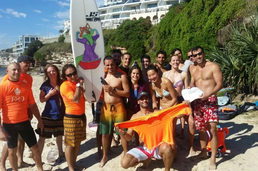 Grupo de estudiantes en la playa con una tabla de surf después de clase