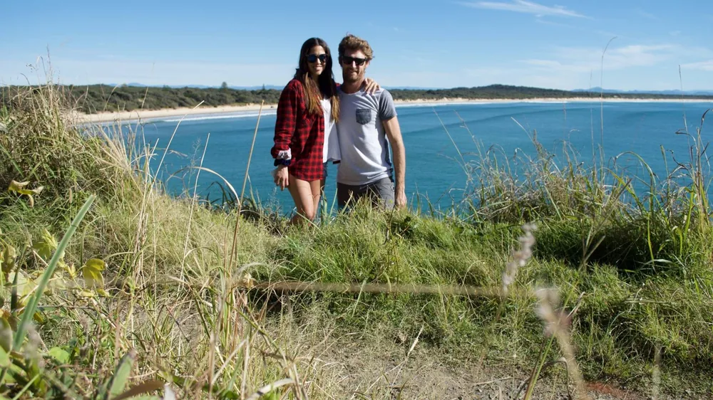 Pareja de estudiantes de Salta sonriendo en un mirador sobre una playa de Australia