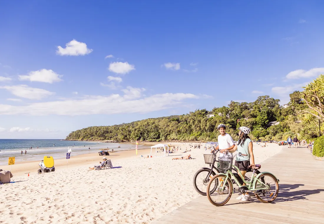 Dos personas con bicis en la playa de Noosa