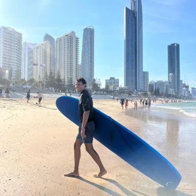 Juan Luque con su tabla de surf en la playa de Surfers Paradise