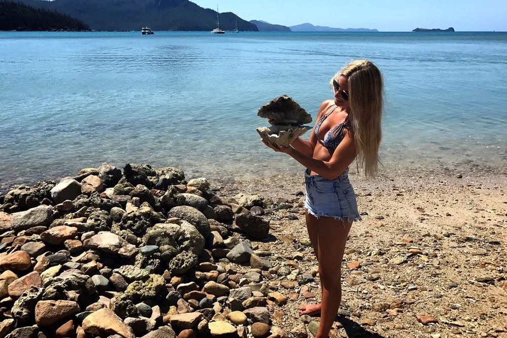Estudiante de Salta con una gran concha en una playa de las Whitsundays