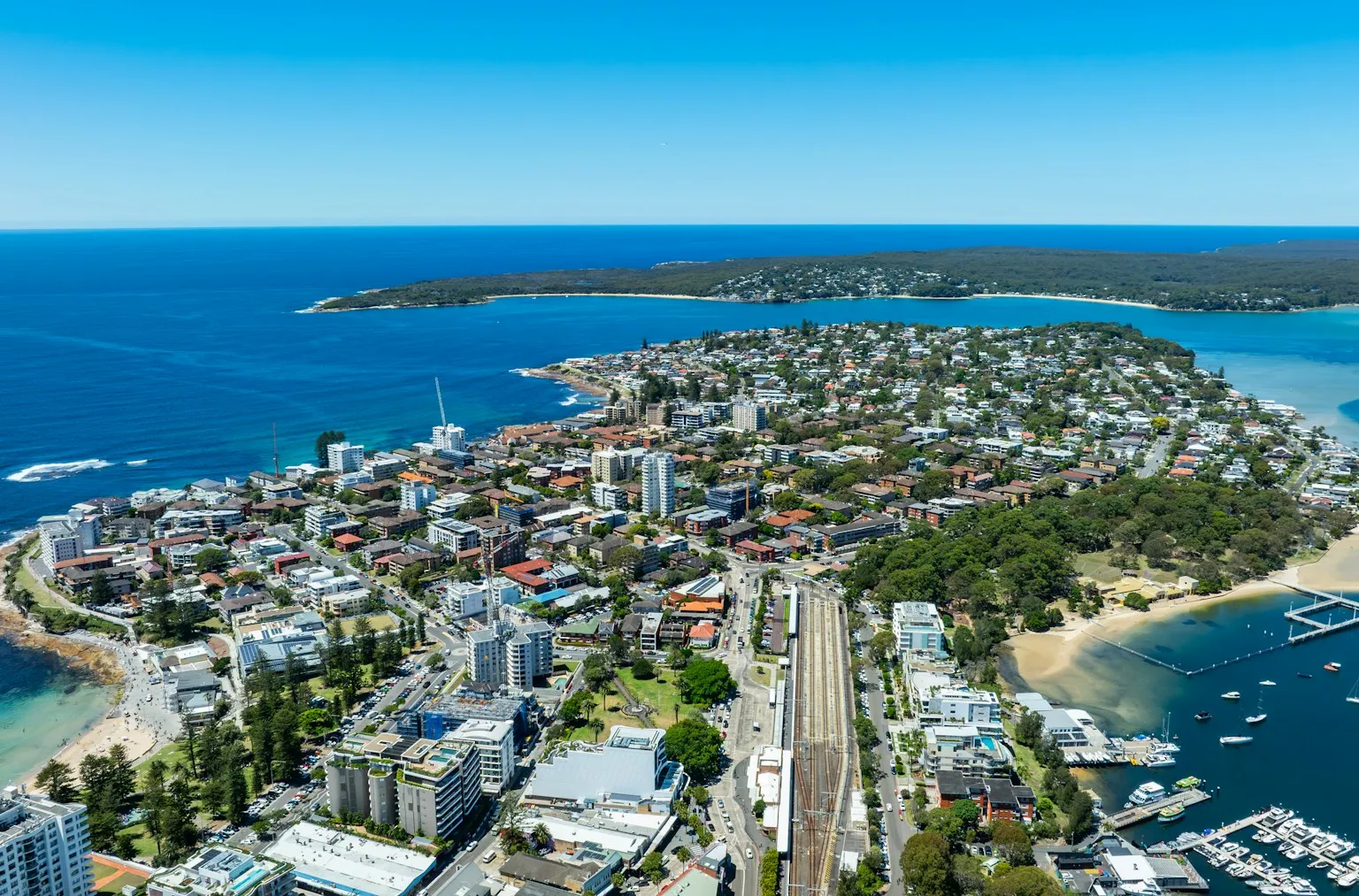 Vista aérea de un barrio de playa de Sydney, con casas, el tren y el mar turquesa